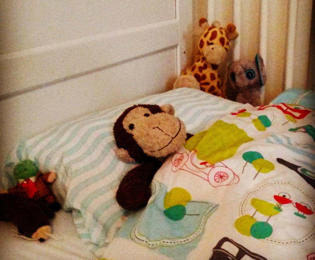 A toy monkey lies in a toddler bed surrounded by other stuffed animals - what to check before you travel with a baby